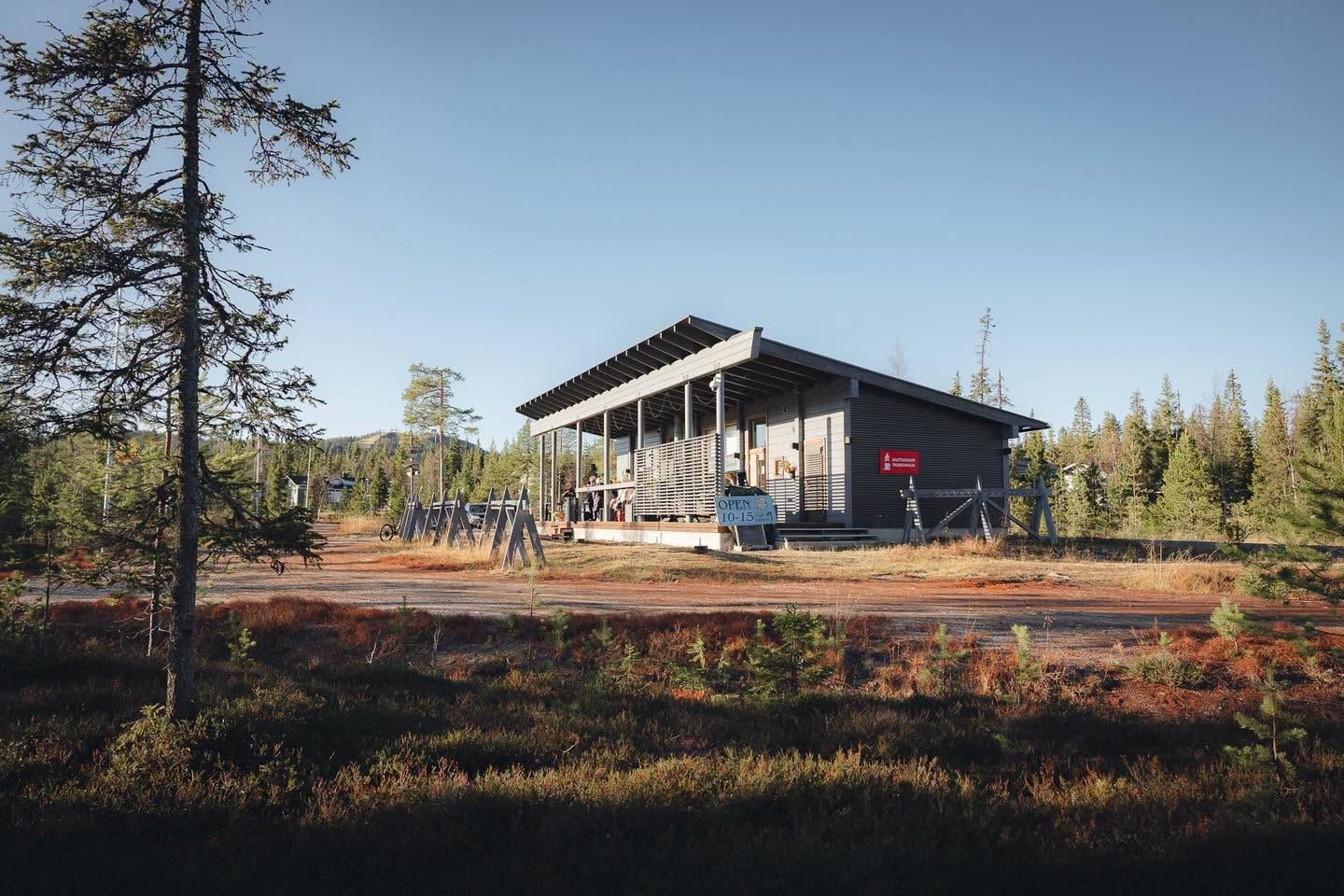 Uuttusuon kahvila syksyllä kirkkaan sinisen taivaan alla, terassilla asiakkaita ja pihalla suksitelineitä.
